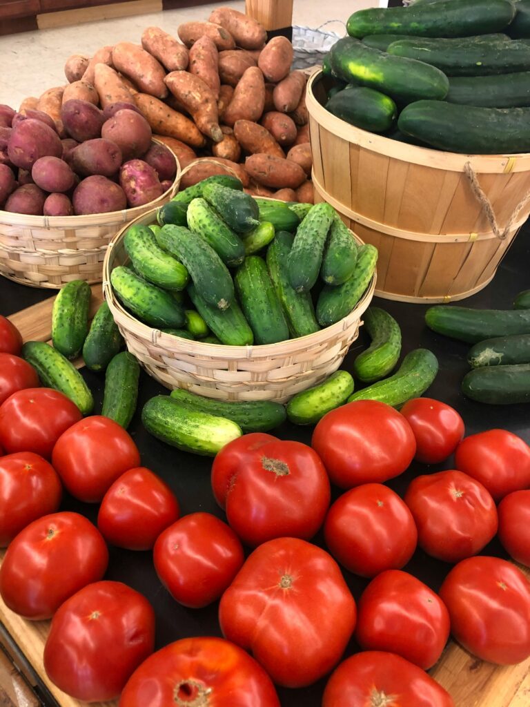 Colorful assortment of fresh vegetables including tomatoes, cucumbers, and sweet potatoes at a market.